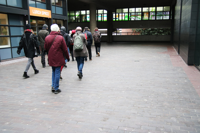 A group of people in winter coats walking down a brick courtyard on the ground level of a building complex.