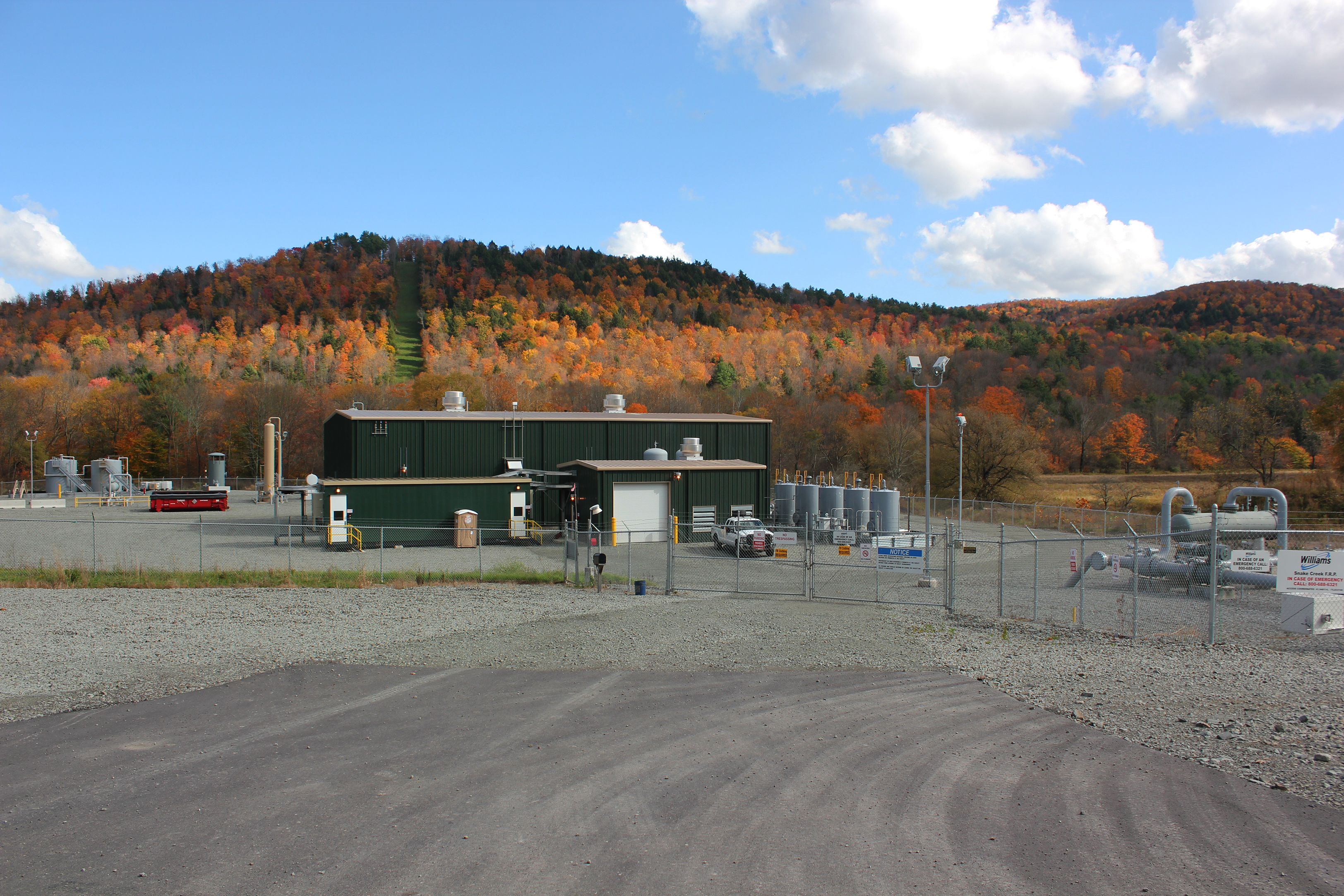 A small commercial building clad in green metal siding, surrounded by a chain-link fence.