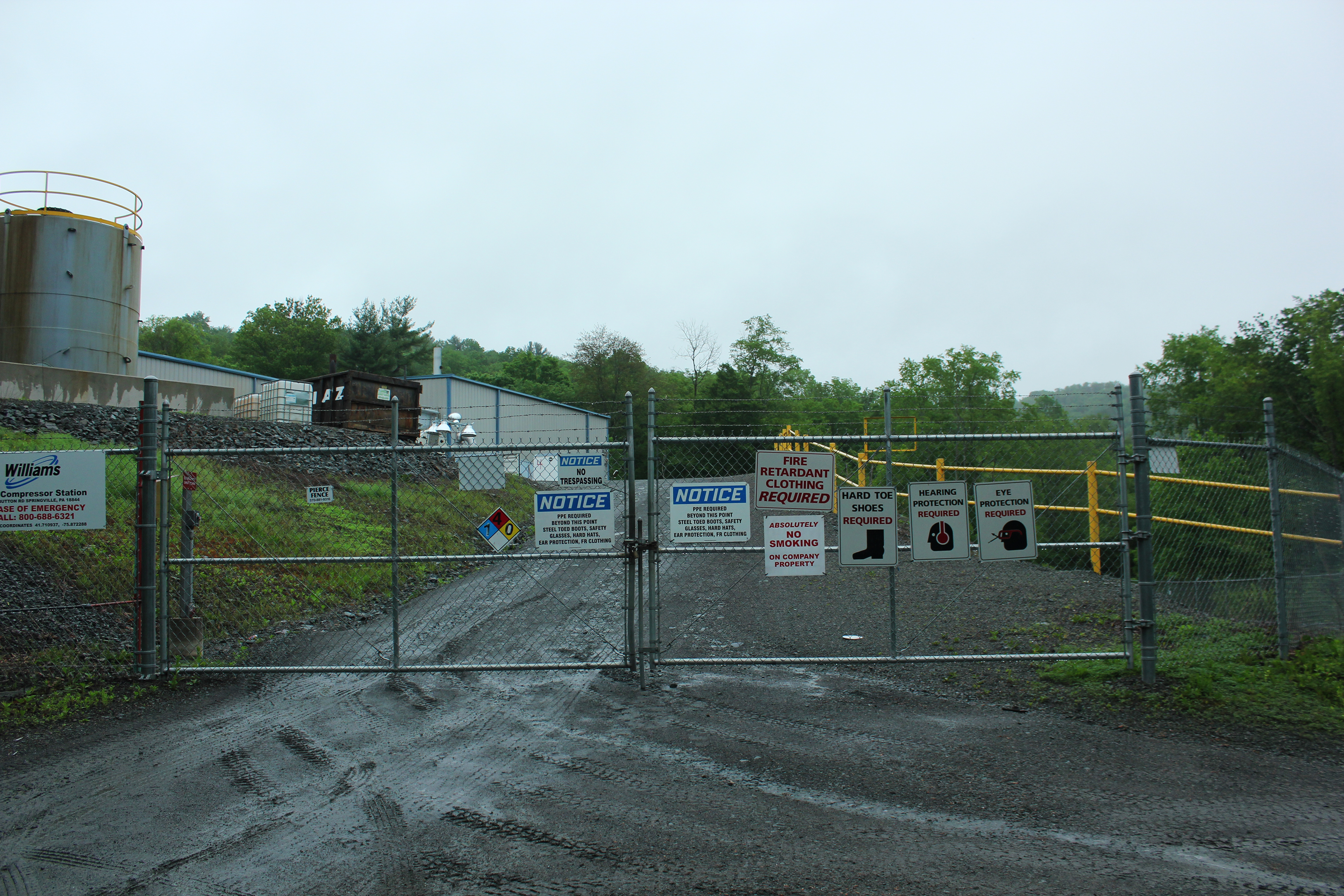 Closed chainlink gate speckled with signs noting various safety warnings and a placard identifying the space as a Williams Compressor Station.
