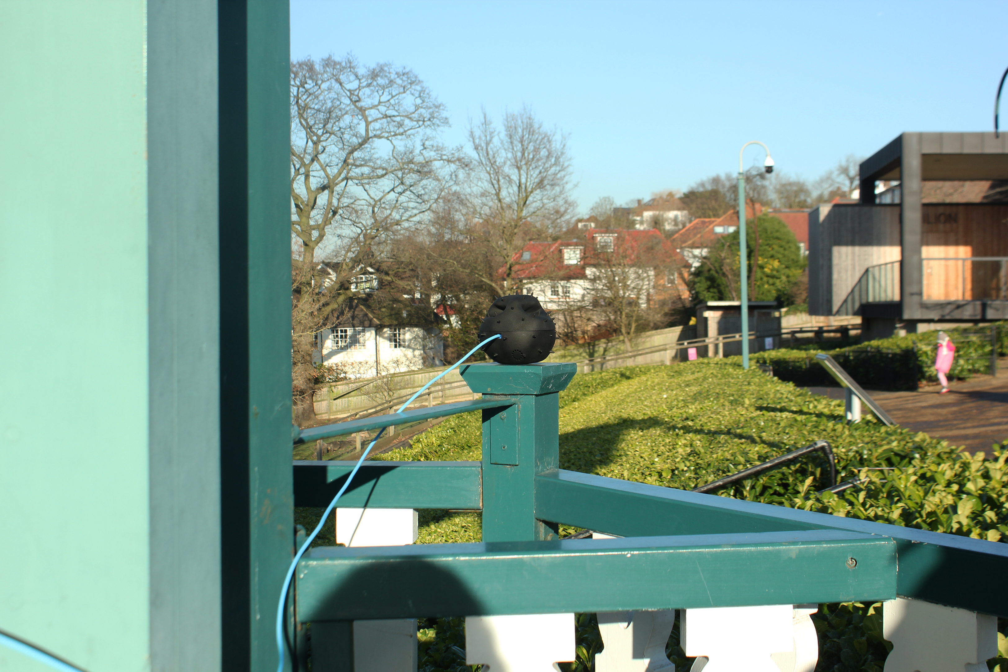 Small spherical black sensor on a green porch banister with a view of a residential neighborhood behind.