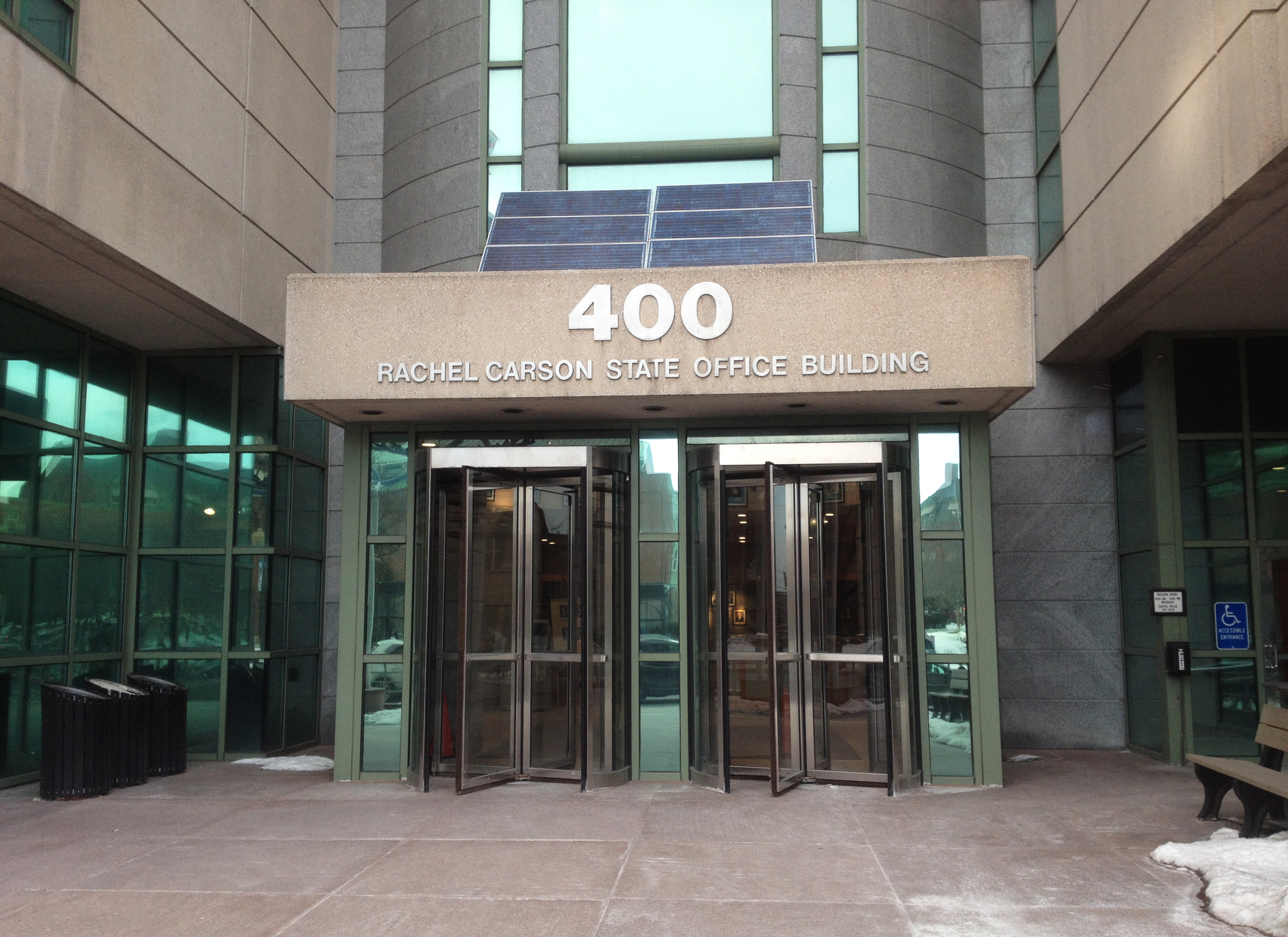 Concrete and glass building facade with two revolving doors side by side beneath an awning reading “400 Rachel Carson State Office Building.”