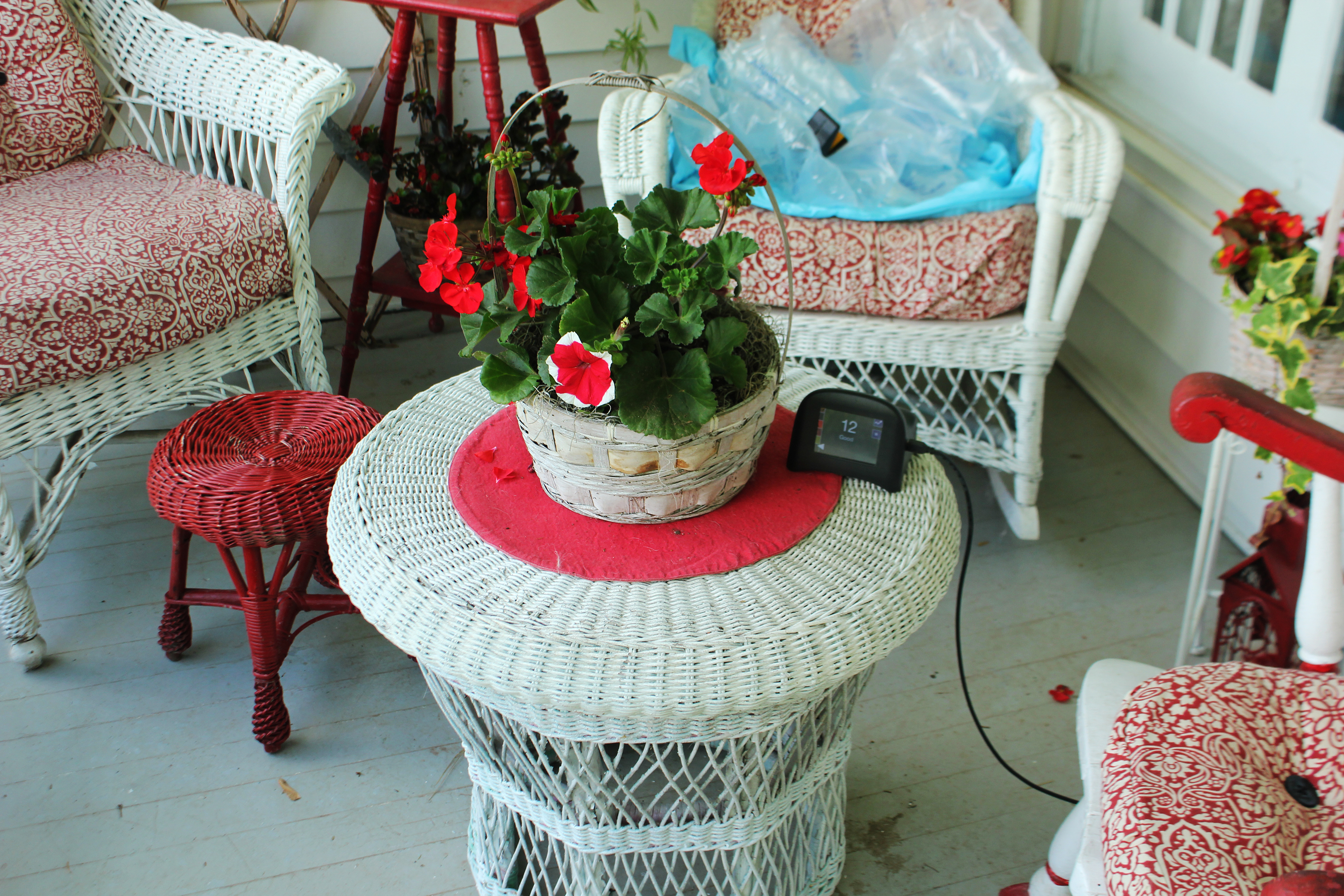 An electronic display sitting on a white wicker coffee table among similar outdoor porch furniture. The display reads “12 Good.”