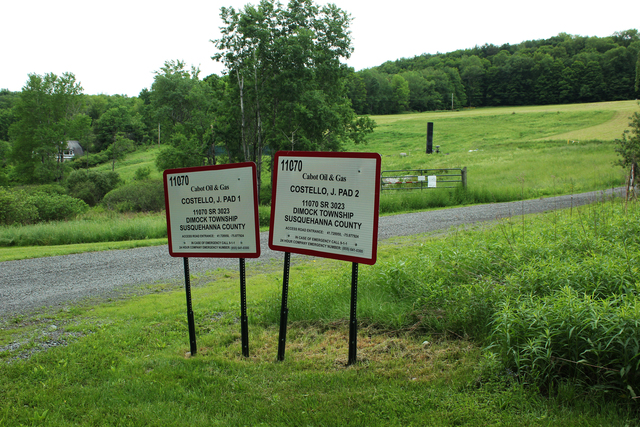 Two signs side by side signs from Cabot Oil and Gas beside a pasture and unpaved path noting Castello, J pads 1 and 2 in Susquehanna County.